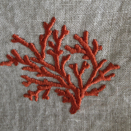 A close-up of coral-shaped embroidery in a rust orange-red thread on a textured light gray linen fabric background.
