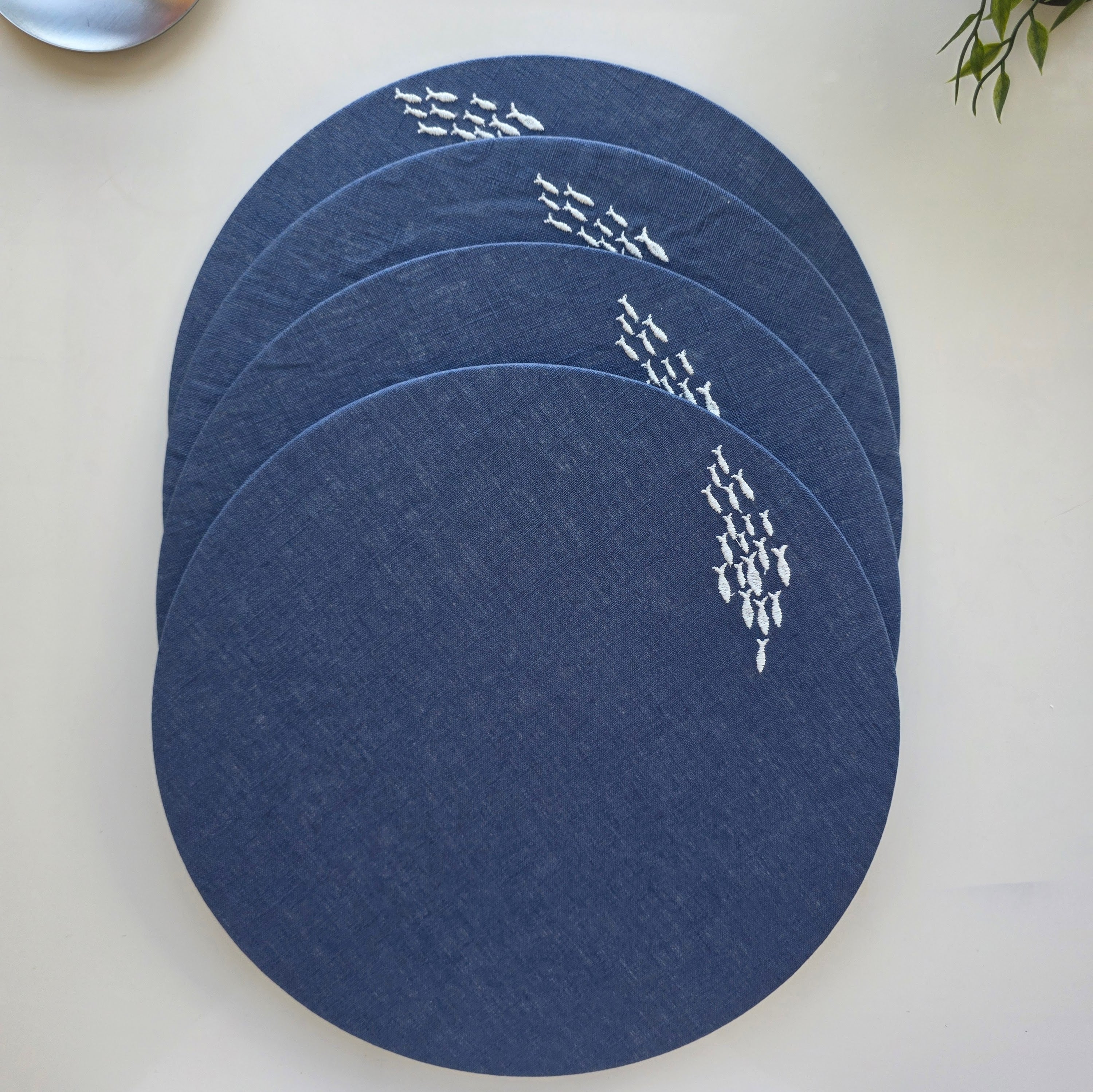 Four round navy blue placemats with white fish patterns, stacked on a light beige surface.