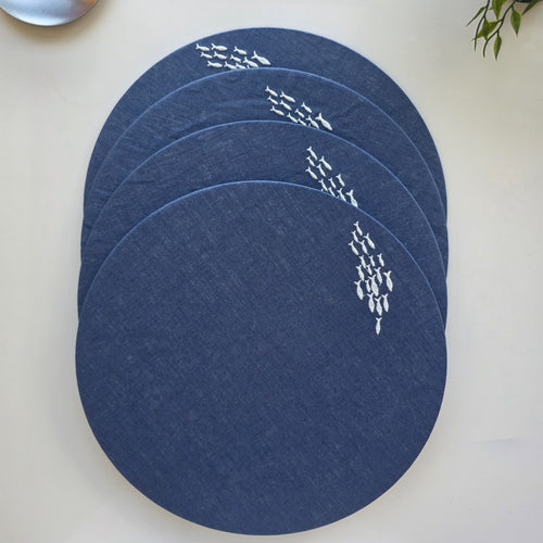 Four round navy blue placemats with white fish patterns, stacked on a light beige surface.