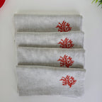 Four folded light gray linen napkins stacked on a white surface, each printed with a small red coral motif near the top.