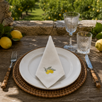 Dining table setting with lemons, glasses, and a napkin with lemon design outdoors. MI RE LA