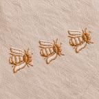 Three embroidered bees on a beige fabric background