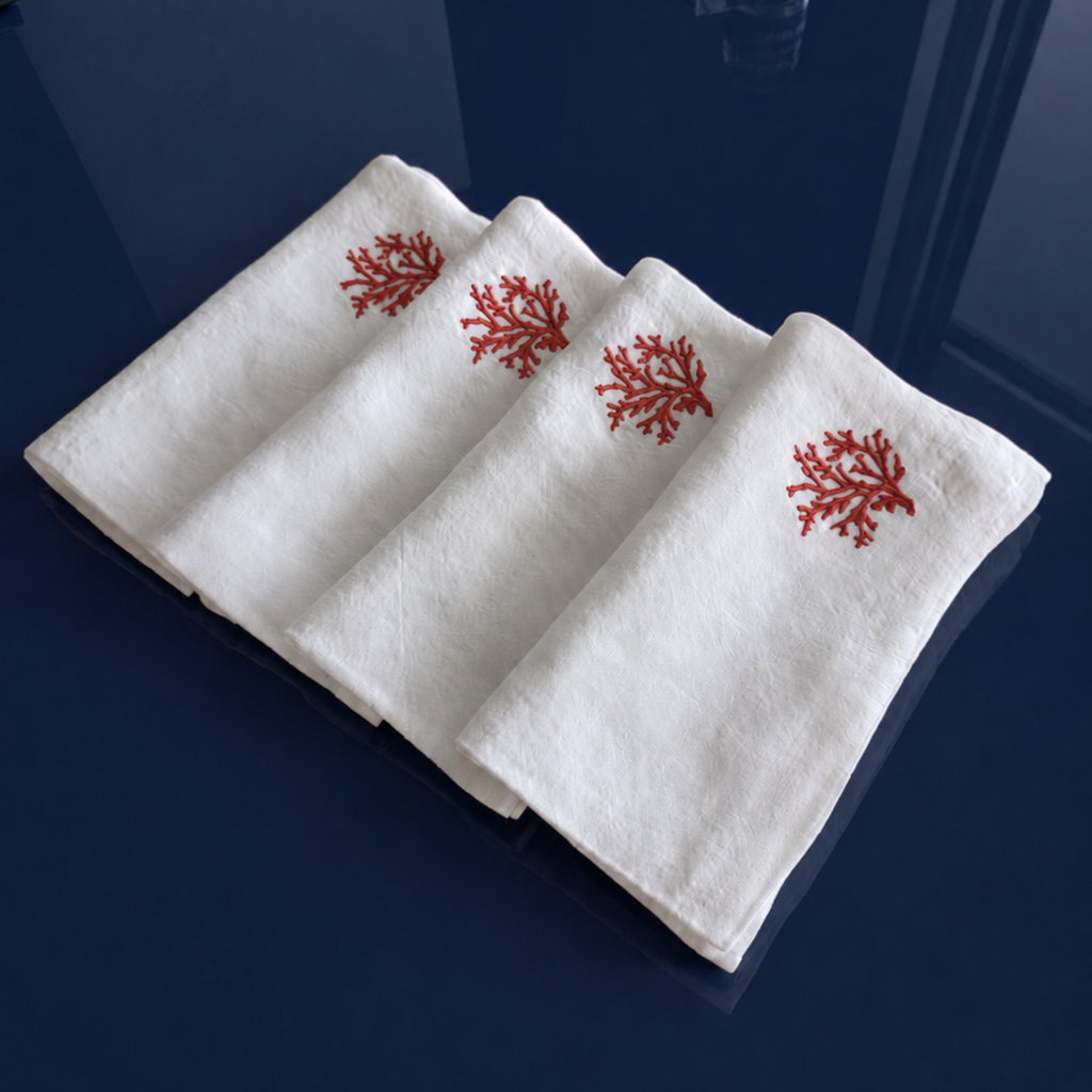 Three folded white towels with red coral embroidery, arranged diagonally on a dark navy blue reflective surface. MI RE LA
