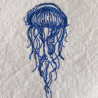 A blue embroidered jellyfish design on a textured off-white fabric background.