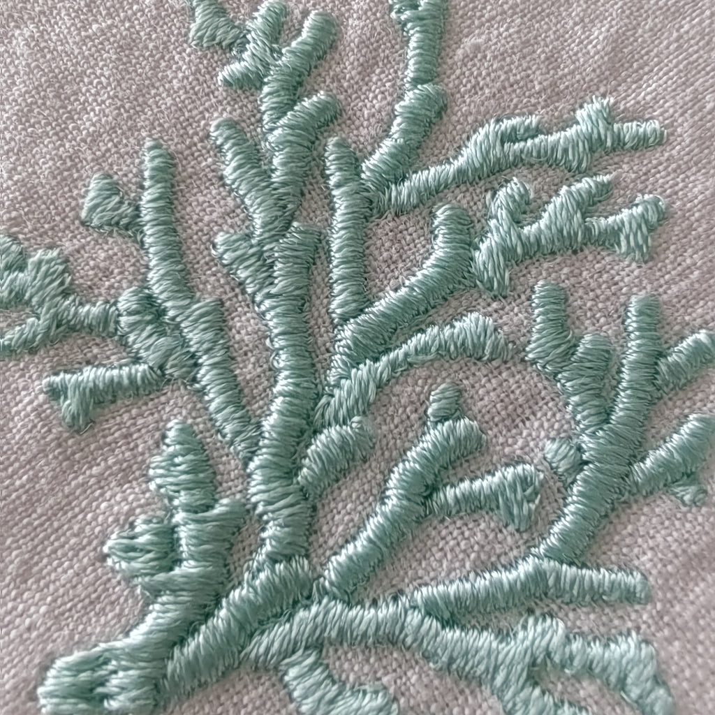 Close-up of a coral branch embroidery design stitched in a light mint green thread on a textured beige fabric MI RE LAbackground.