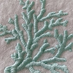 Close-up of a coral branch embroidery design stitched in a light mint green thread on a textured beige fabric MI RE LAbackground.
