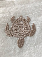 Close-up of a beige embroidered sea turtle design on a textured off-white fabric background.
