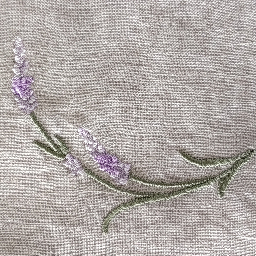 Close-up of a lavender floral embroidery on a light beige linen fabric  MI RE LA background.