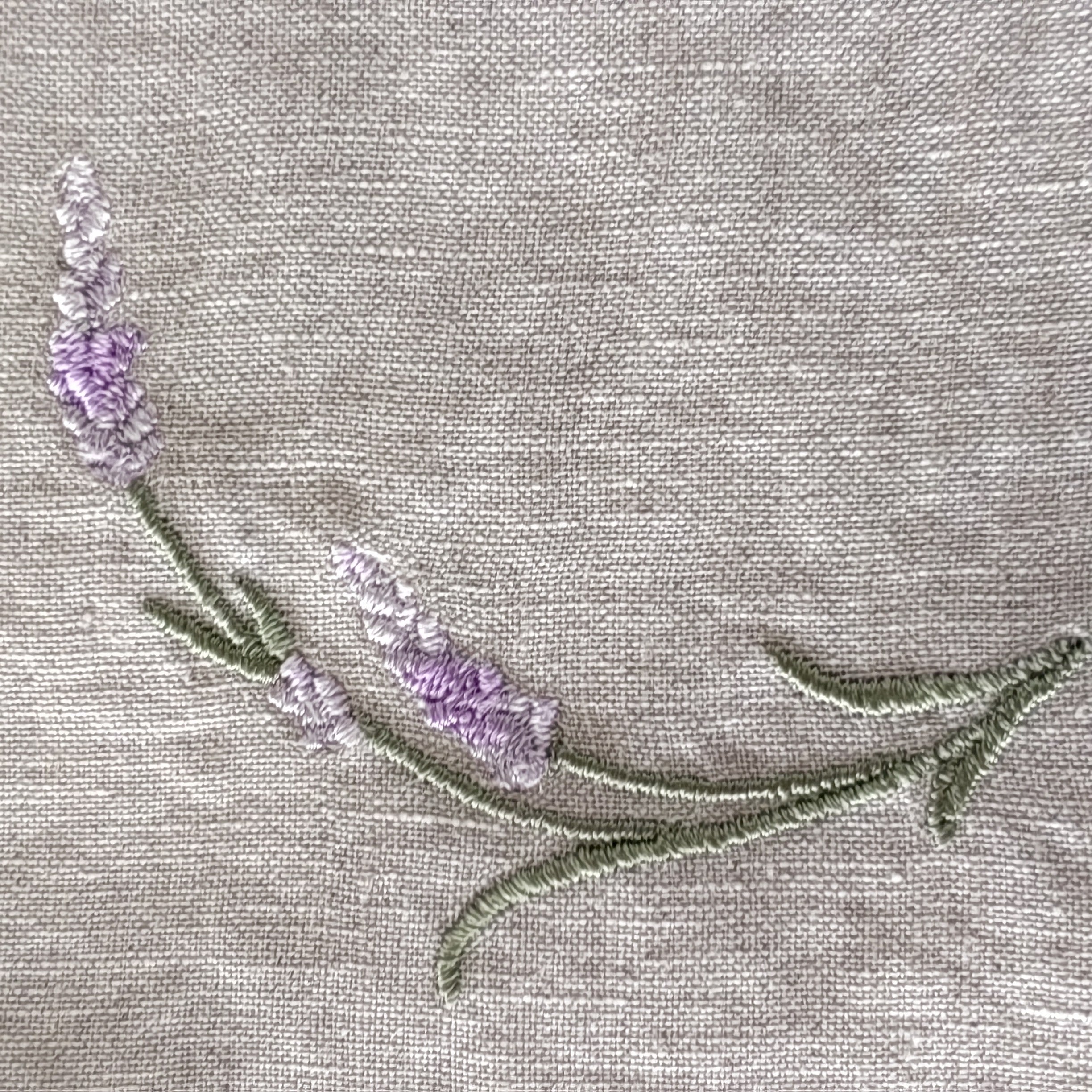 Close-up of a lavender floral embroidery on a light beige linen fabric  MI RE LA background.