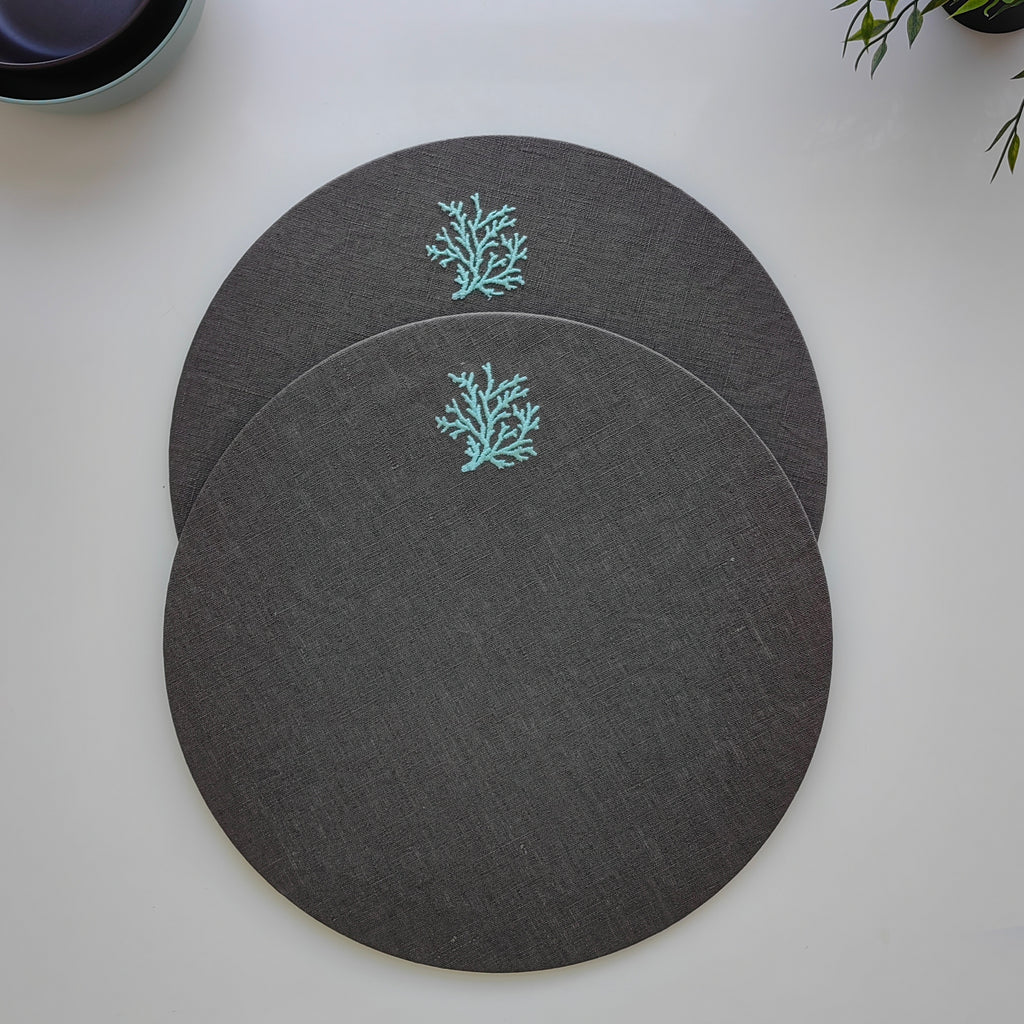 Three round dark gray placemats with a light blue coral design, arranged on a white tabletop.