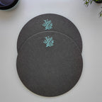 Three round dark gray placemats with a light blue coral design, arranged on a white tabletop.