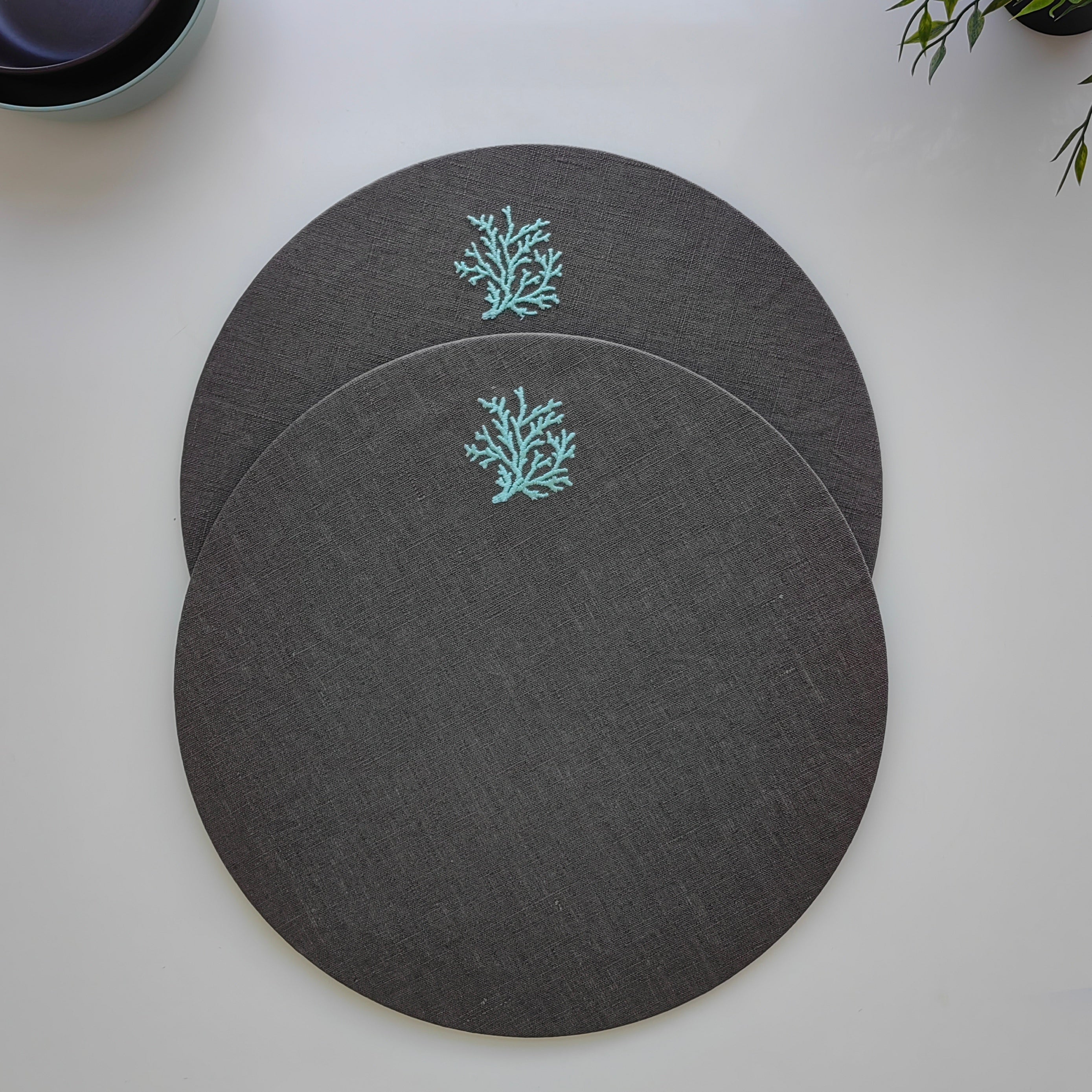 Three round dark gray placemats with a light blue coral design, arranged on a white tabletop.