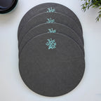 Four round dark gray placemats with a small light blue coral embroidery, arranged in a fan shape on a white surface.