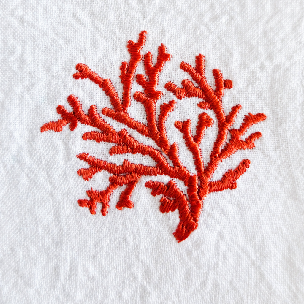A close-up of a coral branch embroidery design stitched in vibrant red-orange thread on a textured white fabric background. MI RE LA