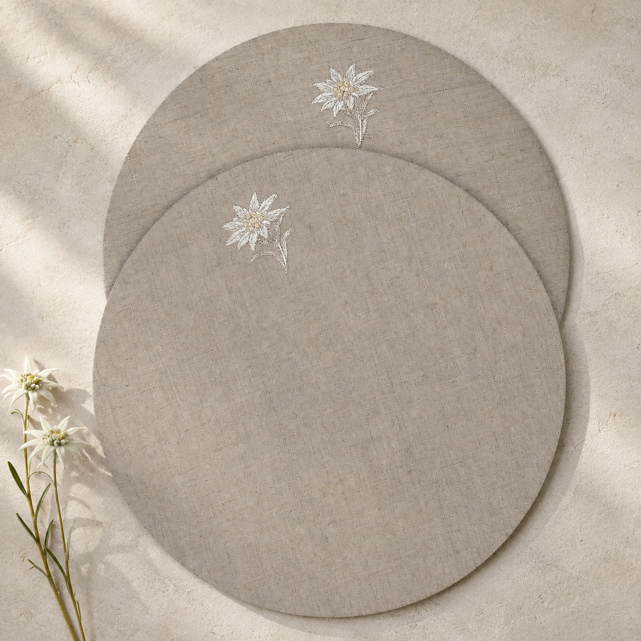 Round coated linen placemats with an embroidered edelweiss on an oatmeal stone ground