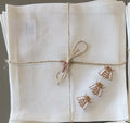A off white linen cocktail napkin tied with twine and a small bead bow, featuring embroidered brown bees on one corner. MI RE LA
