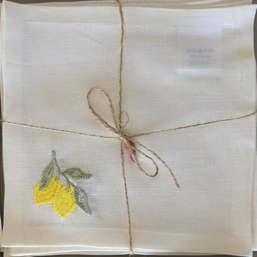 A square off-white linen cockatil napkin with a yellow and green embroidered lemon motif in the upper left corner, wrapped with natural jute twine in a bow. MI RE LA