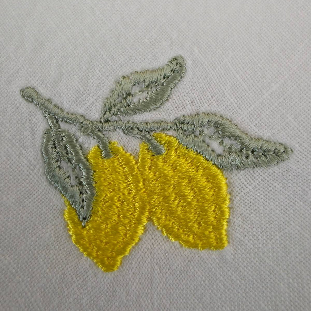 Close view of the lemon embroidery: two tapered yellow lemons on a branch with three sage green leaves, on off-white linen