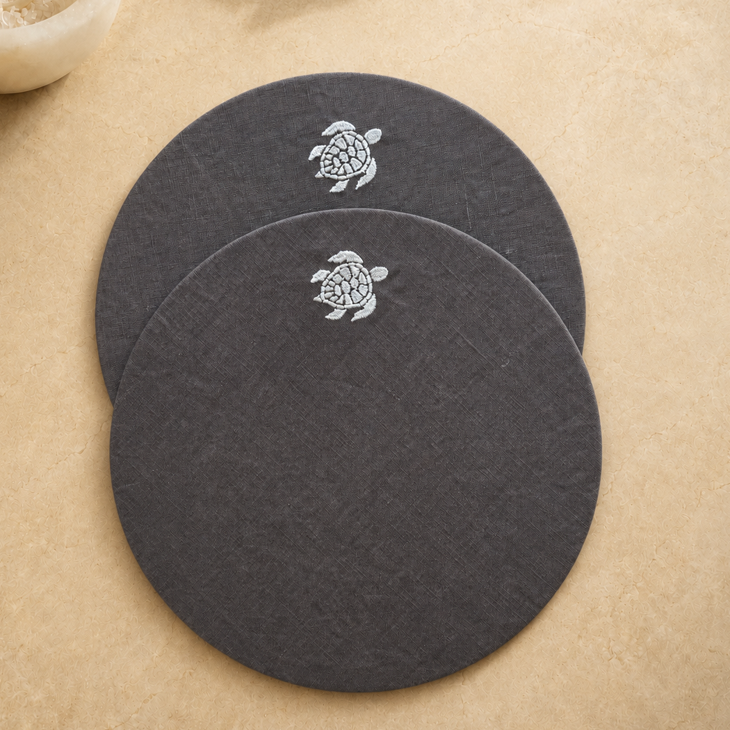 Round coated linen placemats with an embroidered Toscana turtle on a dark taupe ground